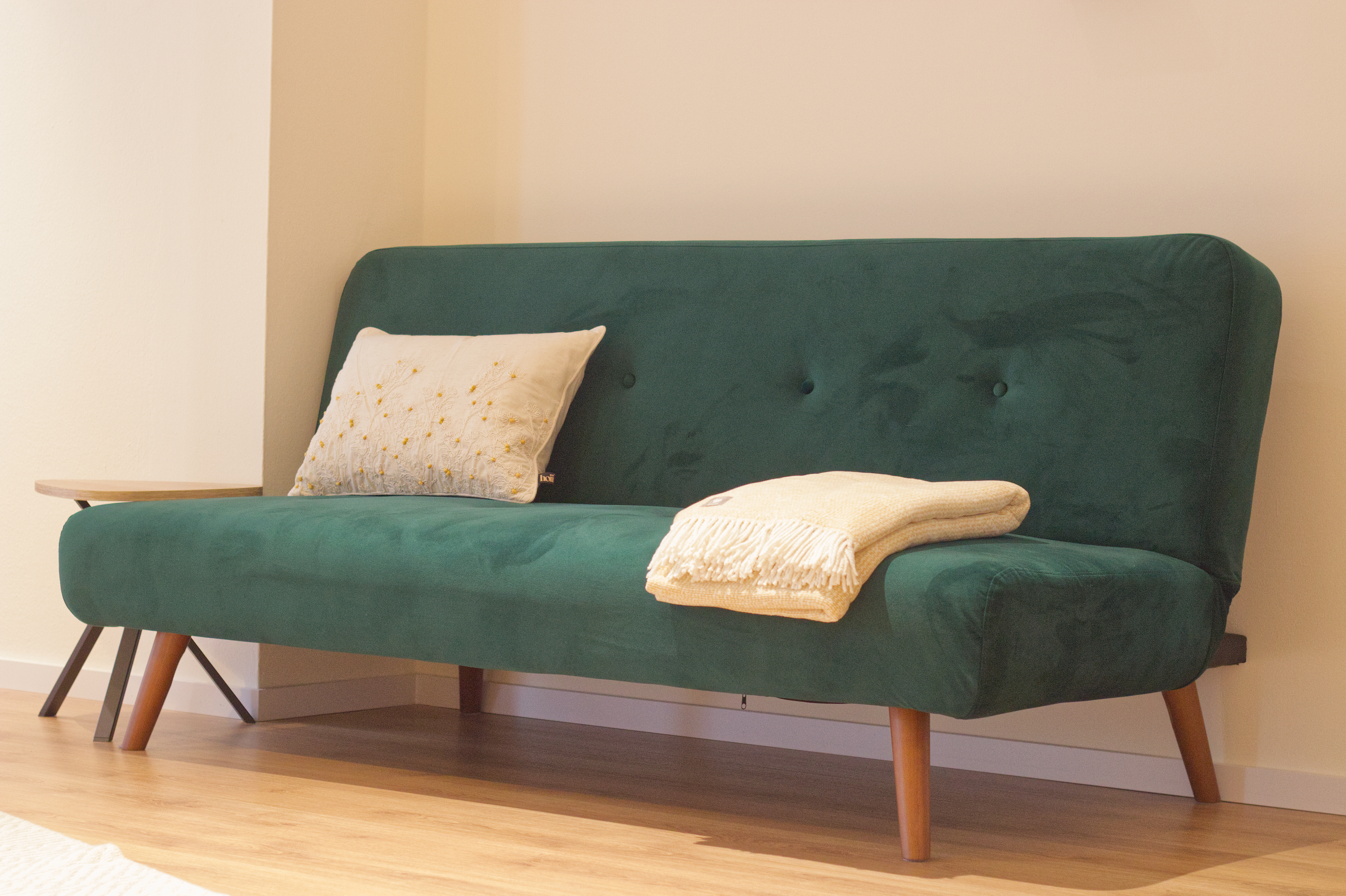 Smaragdgrünes Sofa mit besticktem Wildblumen-Kissen und beiger Wolldecke im Praxisraum